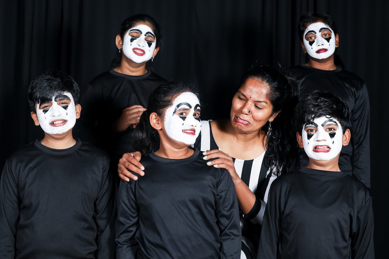 Children and an adult display expressive mime faces during a theatrical performance indoors.