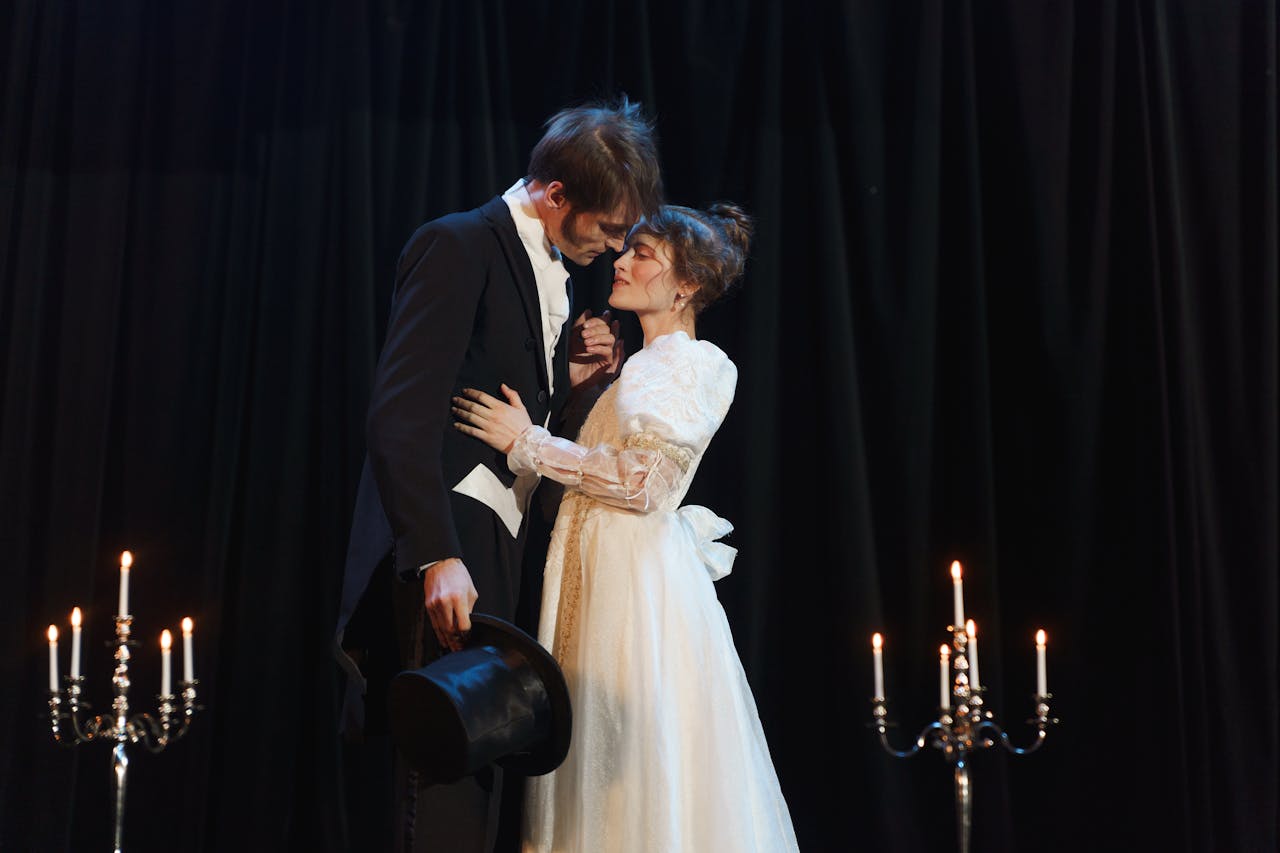 A dramatic romantic scene on stage with a couple in classic costumes surrounded by candlelight.