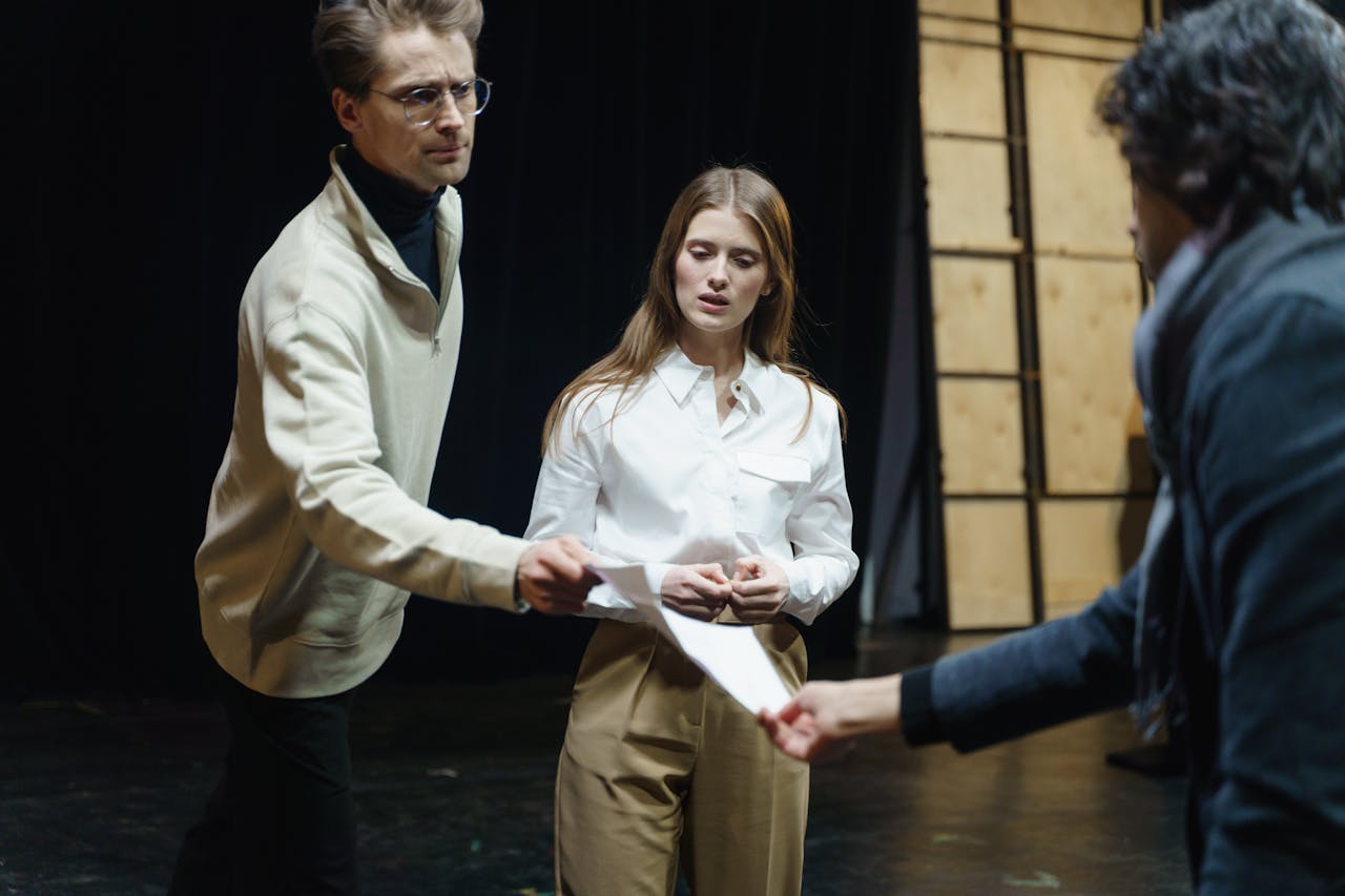Actors engage in a rehearsal, exchanging scripts on stage, embodying theatrical drama and emotion.